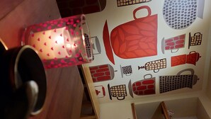 Una cocina con una pared decorada con diversos utensilios y electrodomésticos. Hay una vela sobre la mesa.