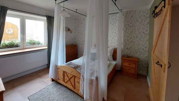 Un dormitorio con cama de madera, una mesita de noche y una ventana con cortinas, además de una puerta con un cartel.
