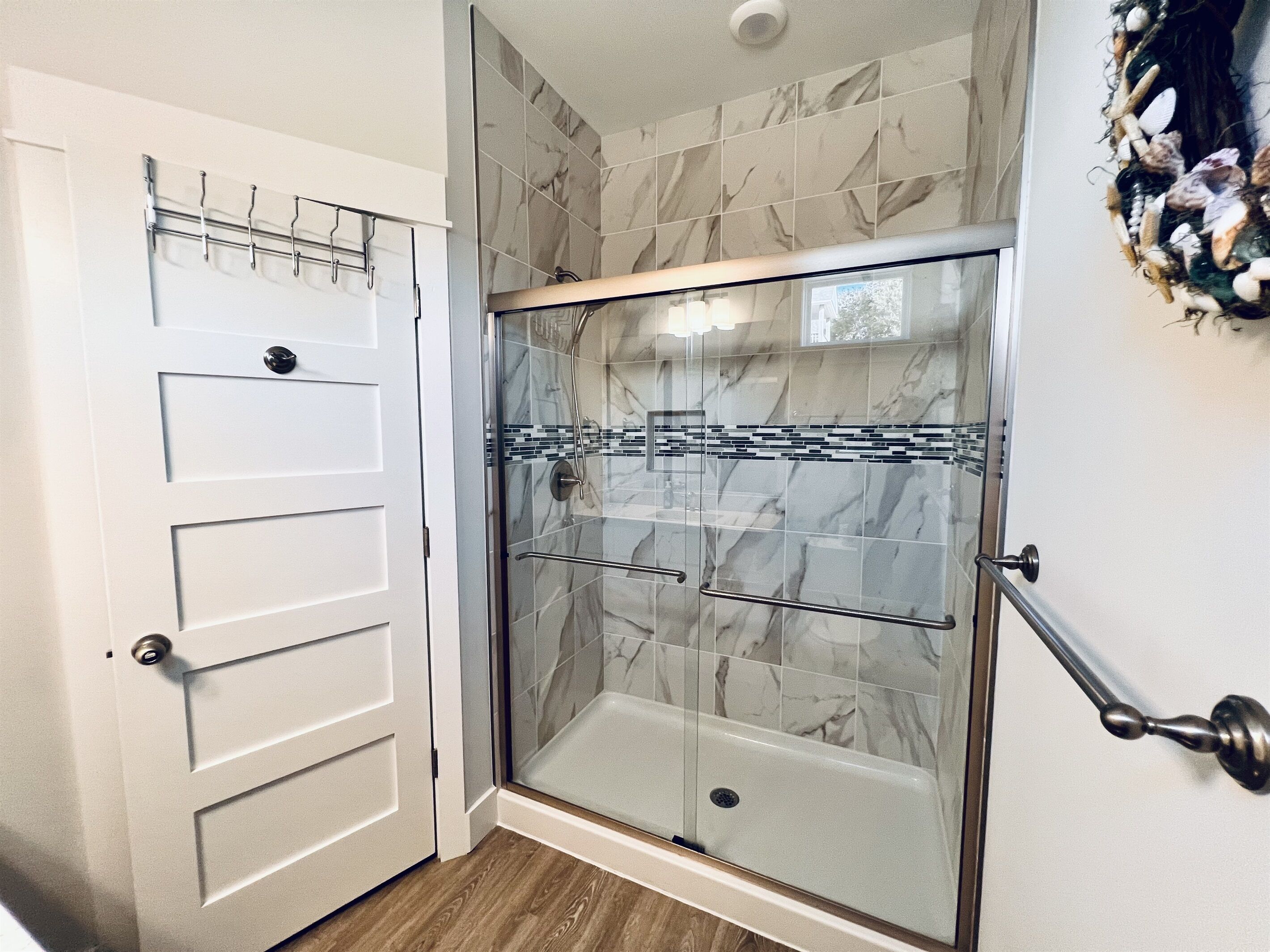 Eine Dusche ohne trittfeste Duschwanne mit Glastüren und einer Marmor-Spritzschutzwand.
