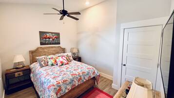 A bedroom with a wooden bed, a ceiling fan, a nightstand with a lamp, a red rug, and a door.