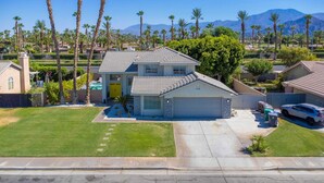 A two-story house with a garage, surrounded by palm trees and a mountain view. - The Great Escape: Pool Home Oasis in the Desert (Indio)