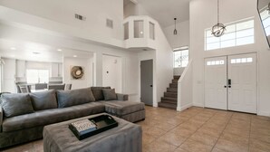 A spacious living area with a grey sectional sofa, a coffee table with a tray, and a staircase leading to a second floor. - The Great Escape: Pool Home Oasis in the Desert (Indio)