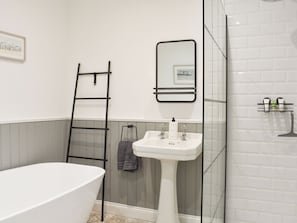 A bathroom with a freestanding bathtub, a pedestal sink, a mirror, and a towel rack.