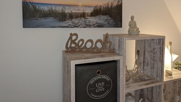 A framed beach scene with a wooden 'Beach' sign and a Buddha statue on a shelf. - Vacation apartment near the beach with sea view (Hohwacht (Ostsee))