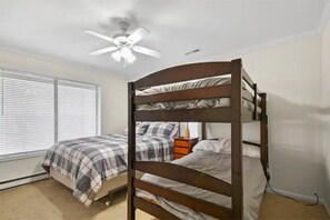 Quarto com cama de solteiro e beliche, ventilador de teto e janela com persianas.