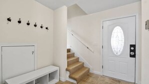 Un couloir avec une porte blanche, un escalier et un banc.