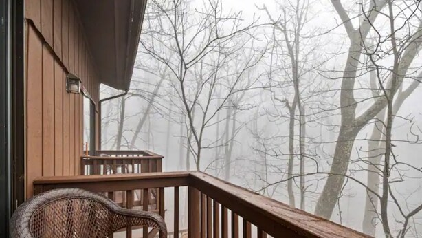 Une terrasse en bois avec un fauteuil en osier, donnant sur une zone boisée où les arbres sont sans feuilles.