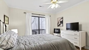 Une chambre à coucher comprenant un lit, un téléviseur, une commode, un ventilateur de plafond et une fenêtre avec des rideaux.