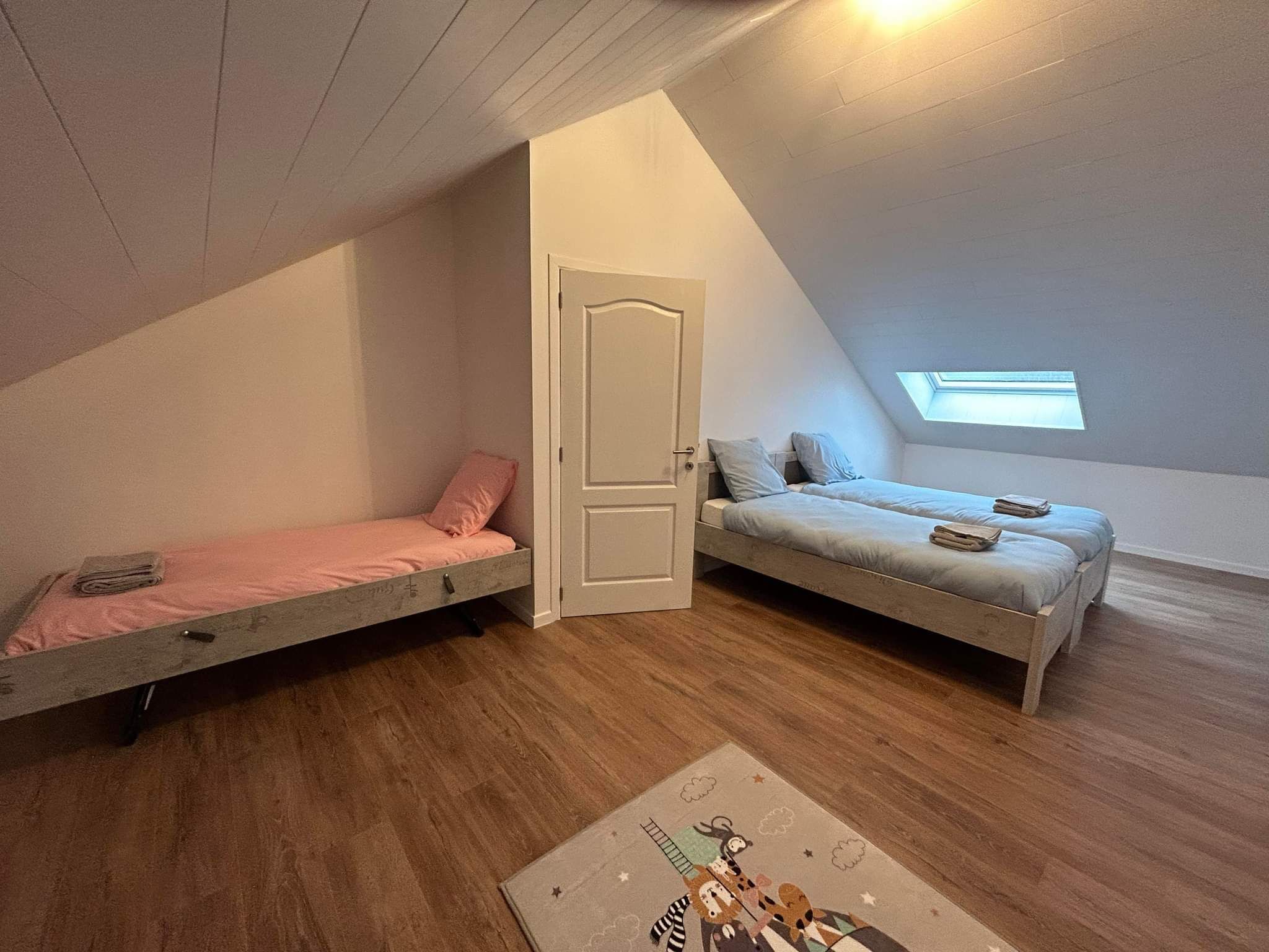A small, attic-style bedroom with two bunk beds, a skylight, and a wooden floor.