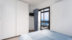 A bedroom with a bed, a wardrobe, a TV, a window with a view, and a chair by the window. - Seafront San Andres (Santa Cruz de Tenerife)