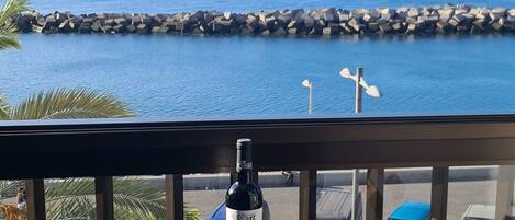 A balcony with a view of the ocean, a bottle of wine, and a glass.
