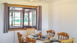 Une salle à manger avec une table dressée pour quatre personnes, des chaises en bois, une fenêtre avec des rideaux et un luminaire au plafond.