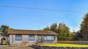 Une maison de plain-pied avec un toit en tuiles, un mur de pierre à l’avant et un ciel d’un bleu limpide.