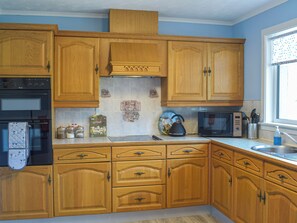 Une cuisine avec des meubles en bois, un four à micro-ondes, une bouilloire et une fenêtre avec des stores.