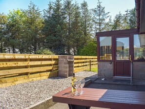 Une terrasse en bois avec une table, une bouteille de vin et deux verres.