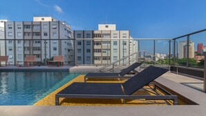 A rooftop pool with lounge chairs and a view of a modern building complex. - Charlie Girassol Vila Madalena (São Paulo)
