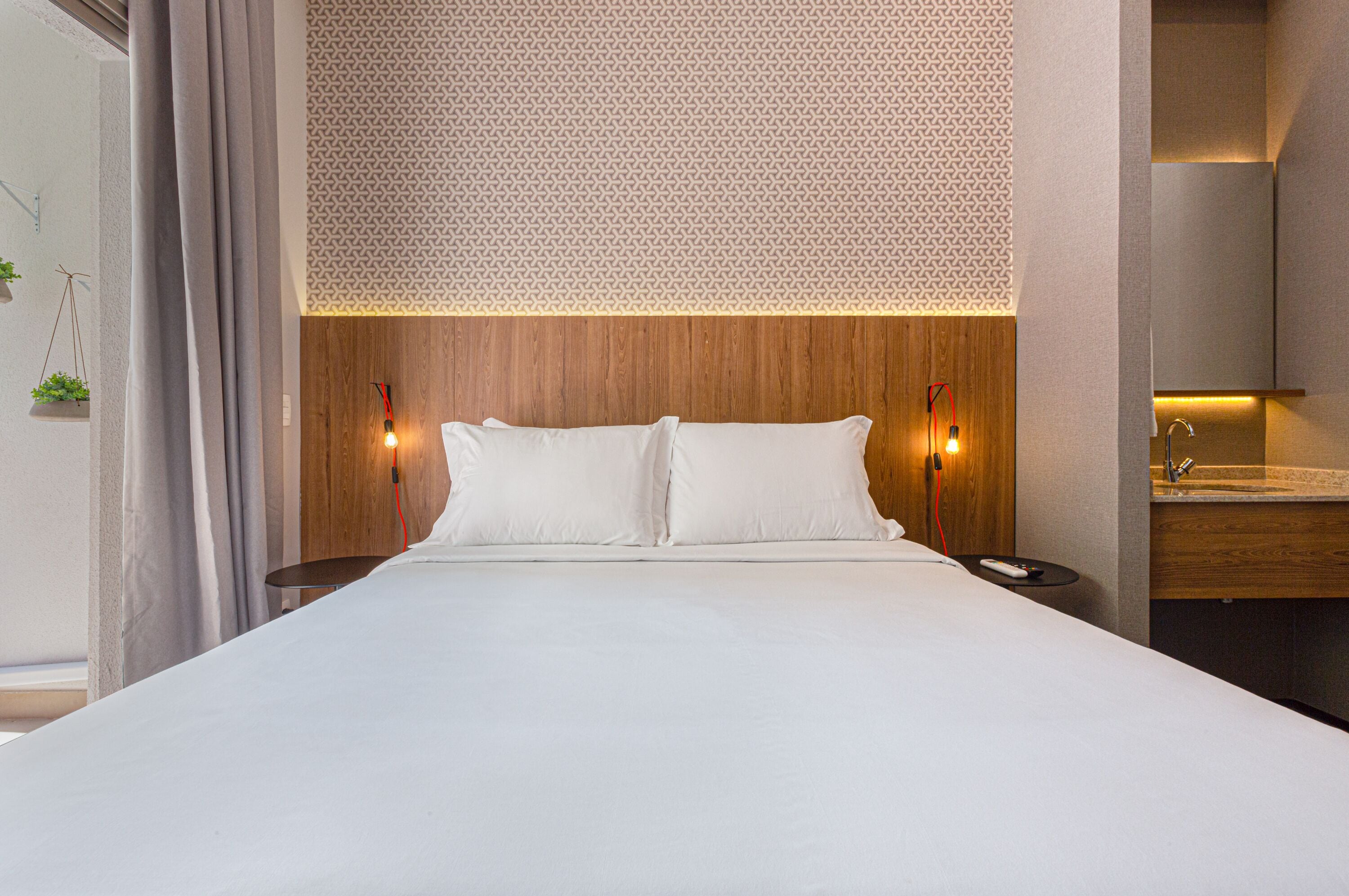 Une chambre d’hôtel moderne dotée d’un grand lit, d’une tête de lit en bois, de deux lampes de chevet et d’une coiffeuse intégrée avec un miroir.