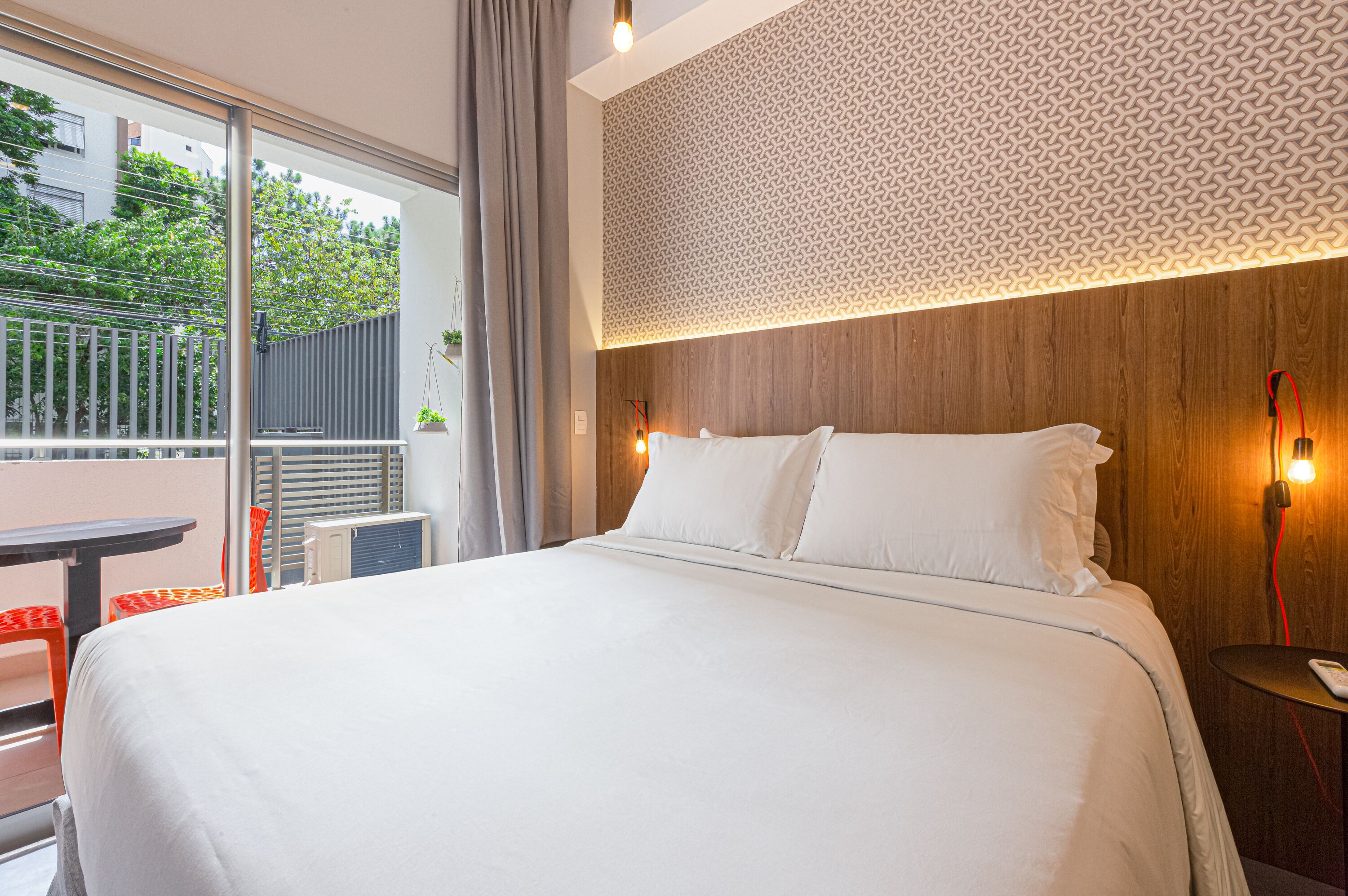 A hotel room with a large bed, a wooden headboard, a patterned wall, and a view of the outdoors.
