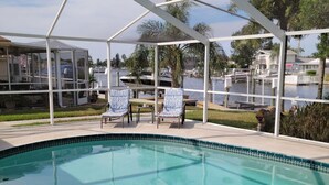 A swimming pool with a covered patio area, outdoor seating, and a view of a marina. - Private Home in desirable Gulf Harbors neighborhood (New Port Richey)
