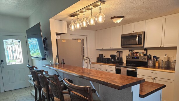 A modern kitchen with a wooden island, bar stools, stainless steel appliances, and a large window. - Private Home in desirable Gulf Harbors neighborhood (New Port Richey)
