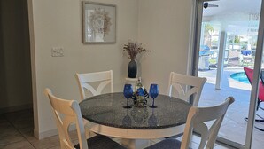 A dining area with a round table, four chairs, a vase with dried plants, and a framed picture on the wall. - Private Home in desirable Gulf Harbors neighborhood (New Port Richey)