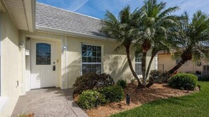 A single-story house with a front door, a small porch, and a well-maintained lawn with palm trees. - Private Home in desirable Gulf Harbors neighborhood (New Port Richey)