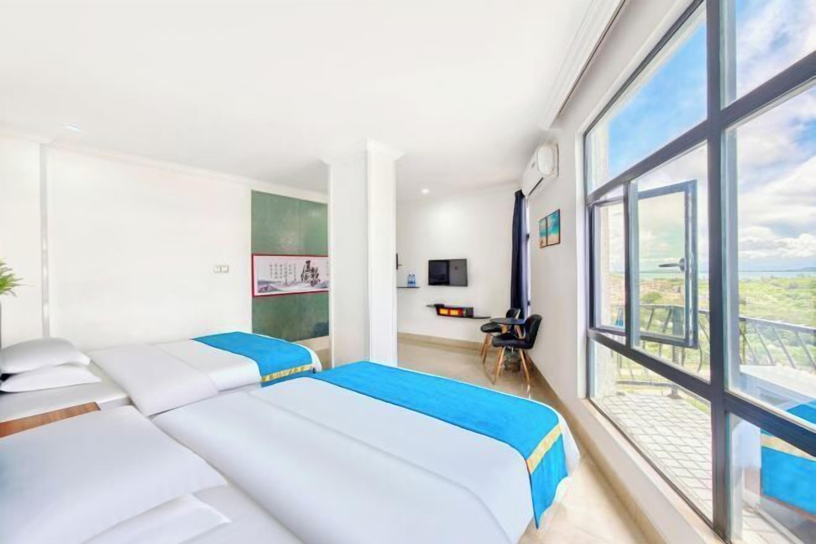 A hotel room with two beds, a desk, a chair, a TV, and large windows.