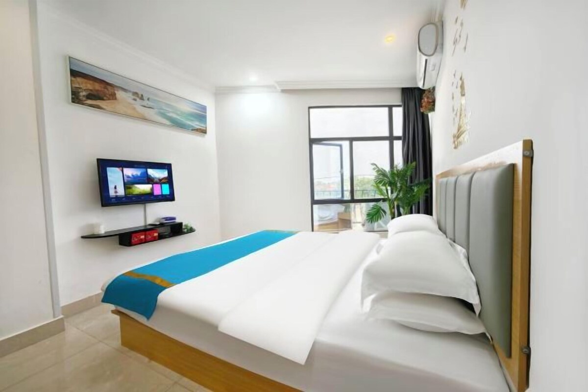 A hotel room with a bed, a television, a window, and a plant.