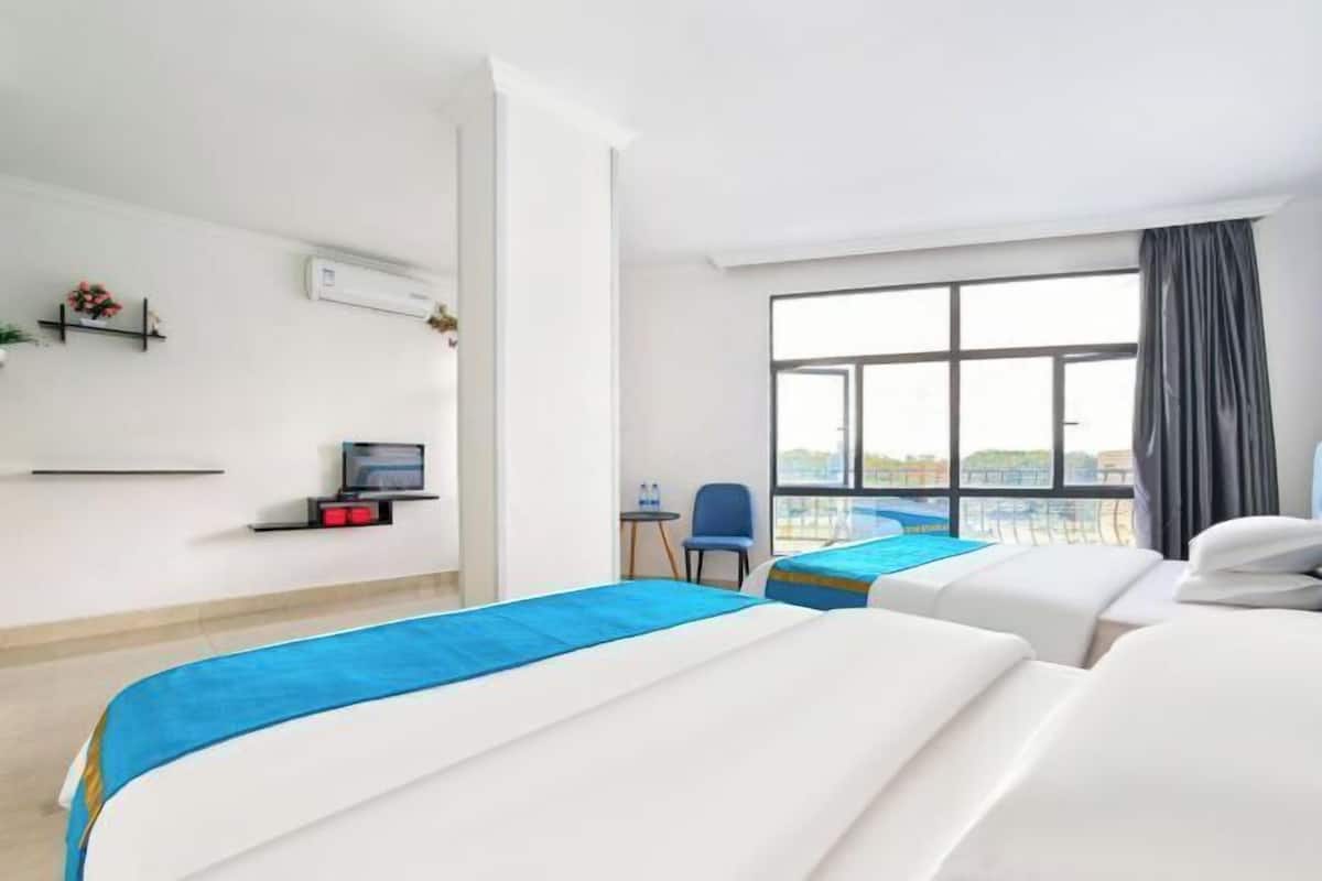A hotel room with two beds, a TV, a small table with a chair, and a large window with a view.