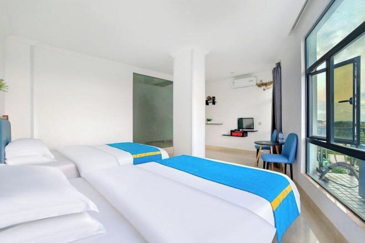A hotel room with two beds, a small seating area, a TV, and a large window.