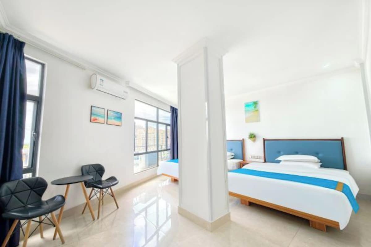 A hotel room with a bed, a small table with chairs, a window with curtains, and a wall-mounted air conditioner.