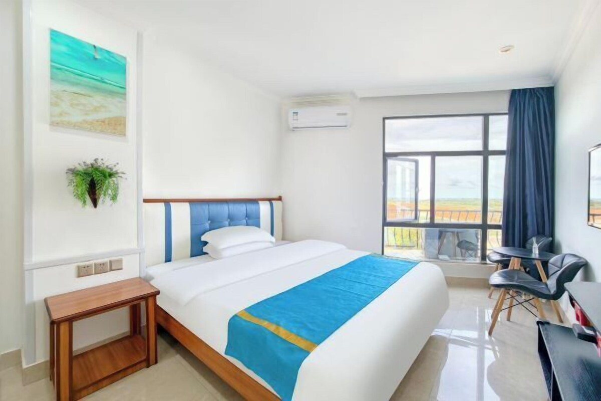 A hotel room with a bed, a desk, a chair, a window with a view, and an air conditioning unit.