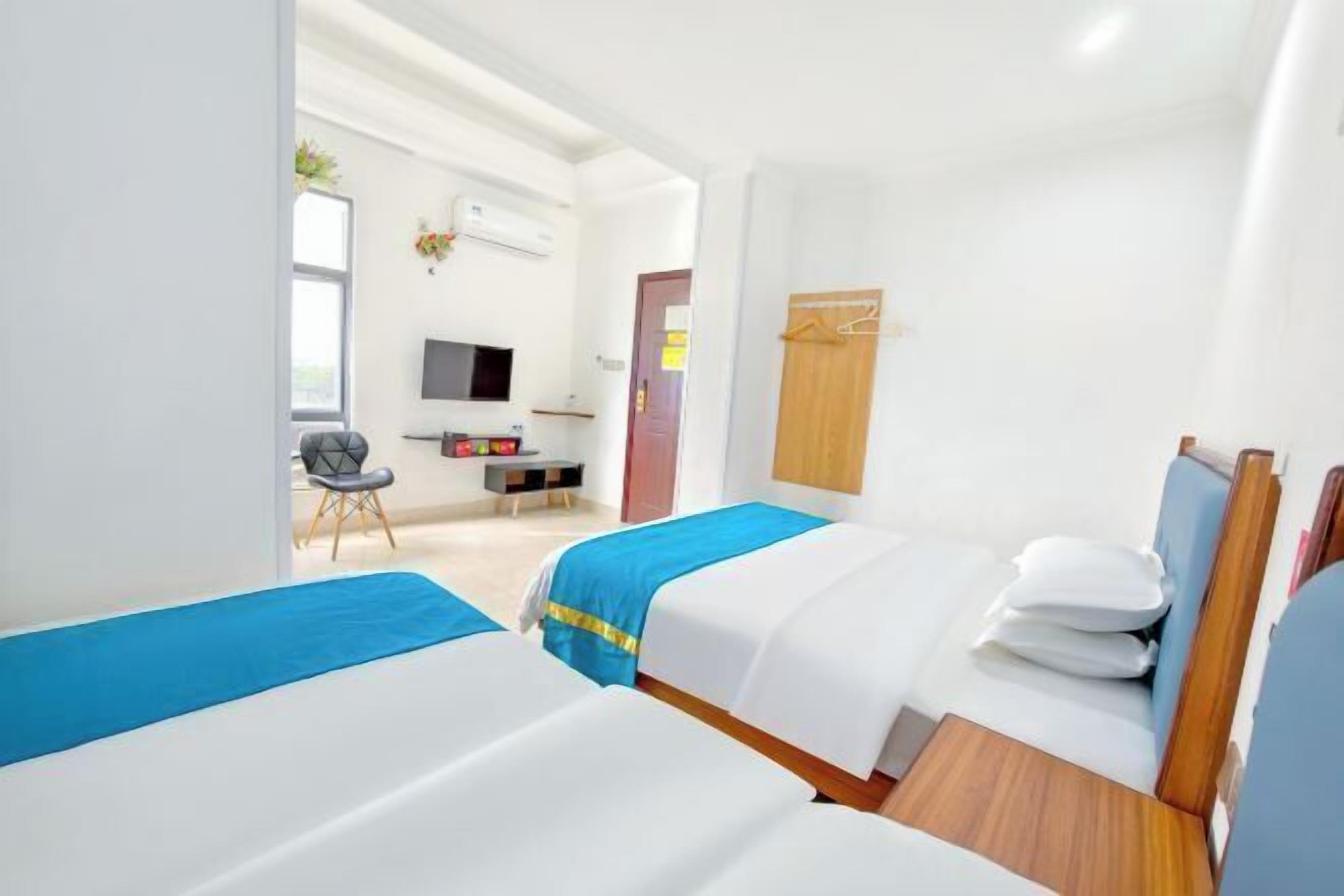 A hotel room with two beds, a desk, a chair, a TV, and a wardrobe.