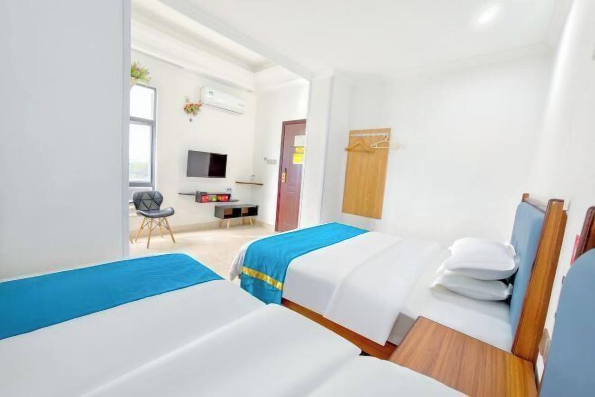 A hotel room with two beds, a desk, a chair, a TV, and a wardrobe.
