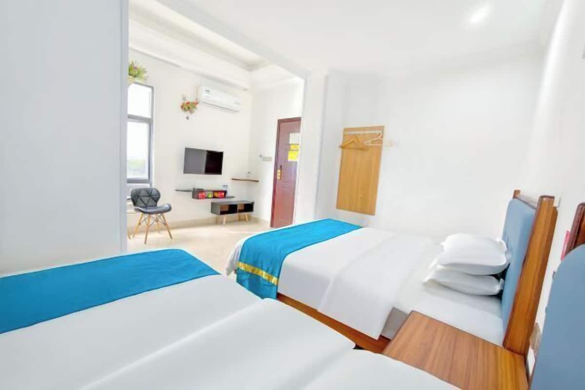 A hotel room with two beds, a desk, a chair, a TV, and a wardrobe.