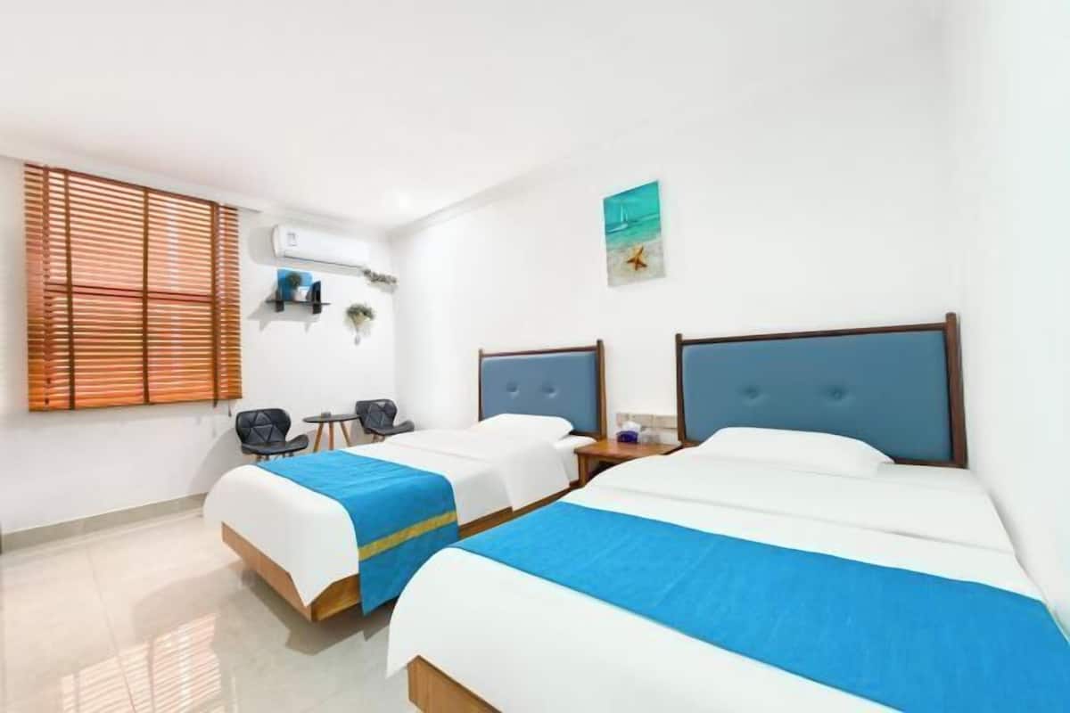 A hotel room with two beds, a desk, a chair, and a window with blinds.