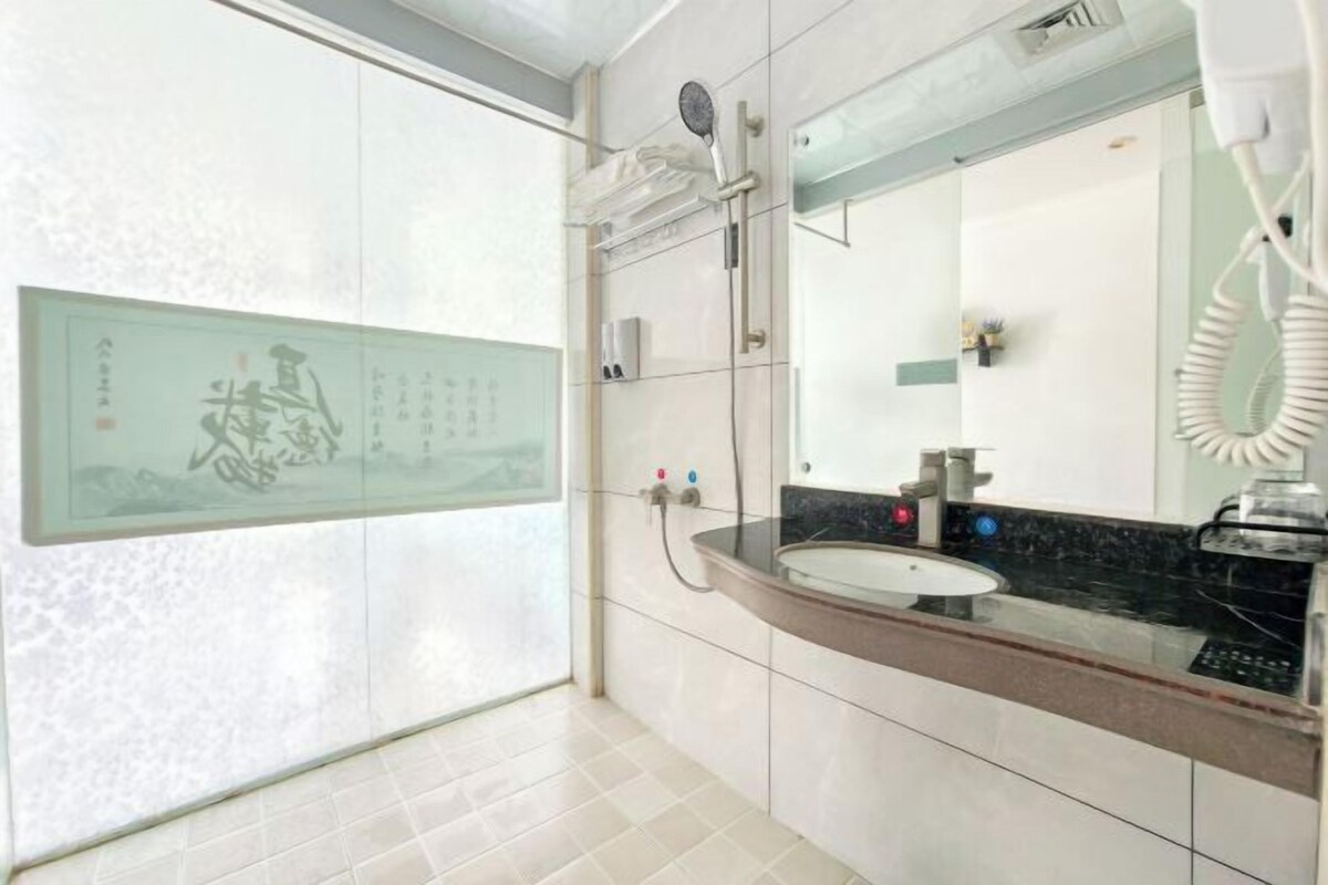 A bathroom with a large mirror, a sink, a shower, and a wall-mounted artwork.