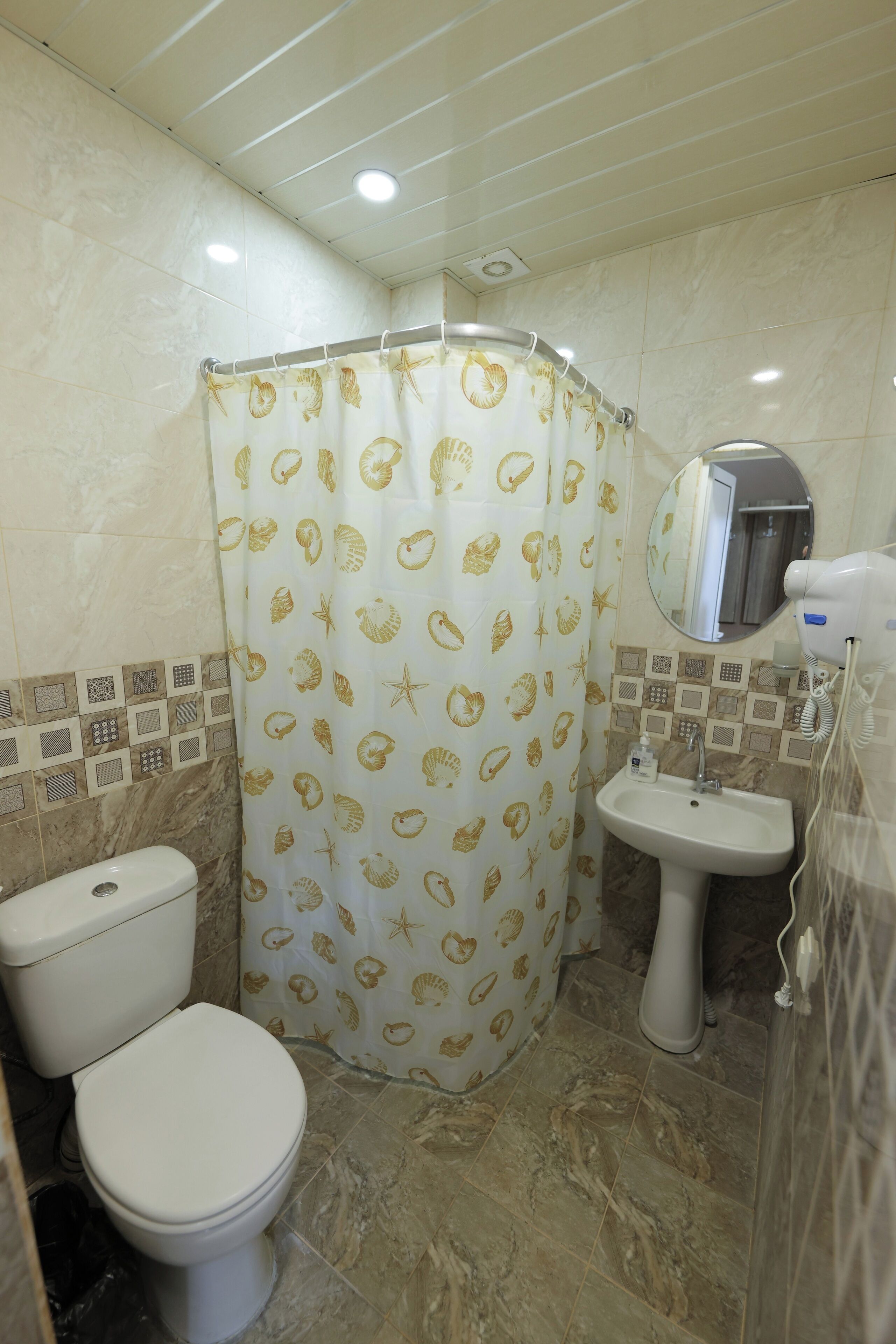 A bathroom with a toilet, sink, and shower curtain with a shell pattern.