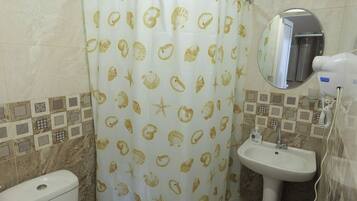 A bathroom with a toilet, sink, and shower curtain with a shell pattern.