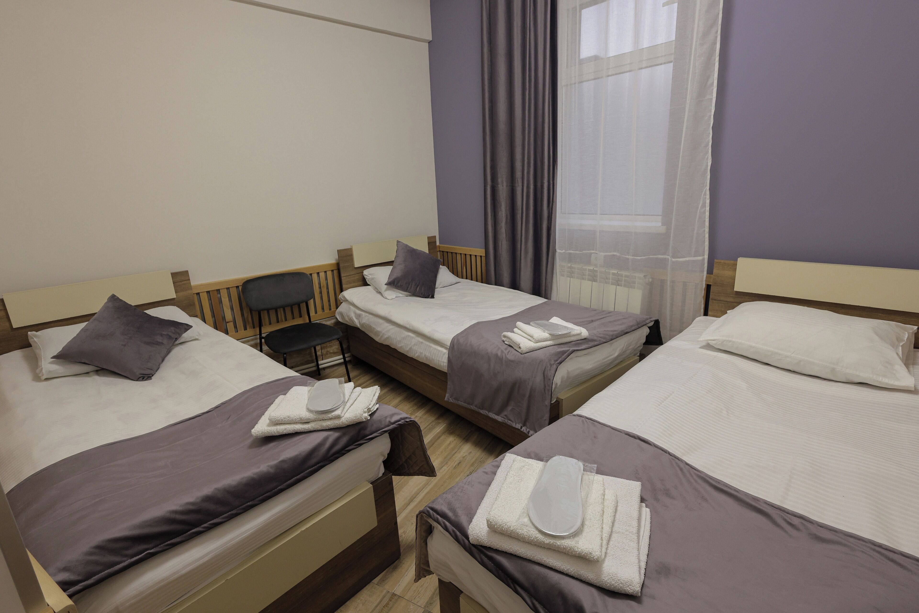 A hotel room with three single beds, a desk, and a chair.