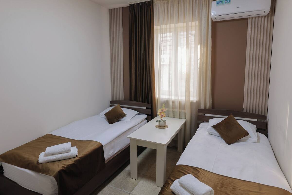 Una habitación de hotel con dos camas, una mesita pequeña, una lámpara en el techo y un aire acondicionado.