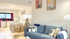 Una sala de estar moderna con un sofá azul, una mesa de centro de madera y un comedor con una mesa y sillas blancas.