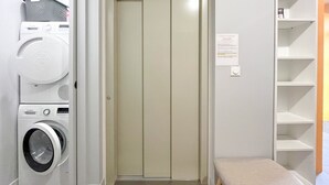 Un lavadero con una lavadora Bosch, una puerta cerrada y un pequeño banco.
