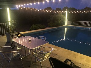An outdoor pool area with a metal table and chairs, surrounded by string lights.