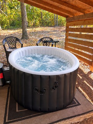 Un jacuzzi bajo una pérgola de madera, con sillas y una mesa cerca.