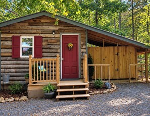 A log cabin with a red door, a porch with steps, and a covered area to the right.