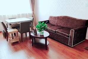A living room with a sofa, a small round table with a plant, a wooden stool, and a dining table with chairs.