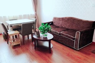 A living room with a sofa, a small round table with a plant, a wooden stool, and a dining table with chairs.