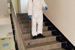 Een persoon in een wit pak en blauwe handschoenen staat op een trap.