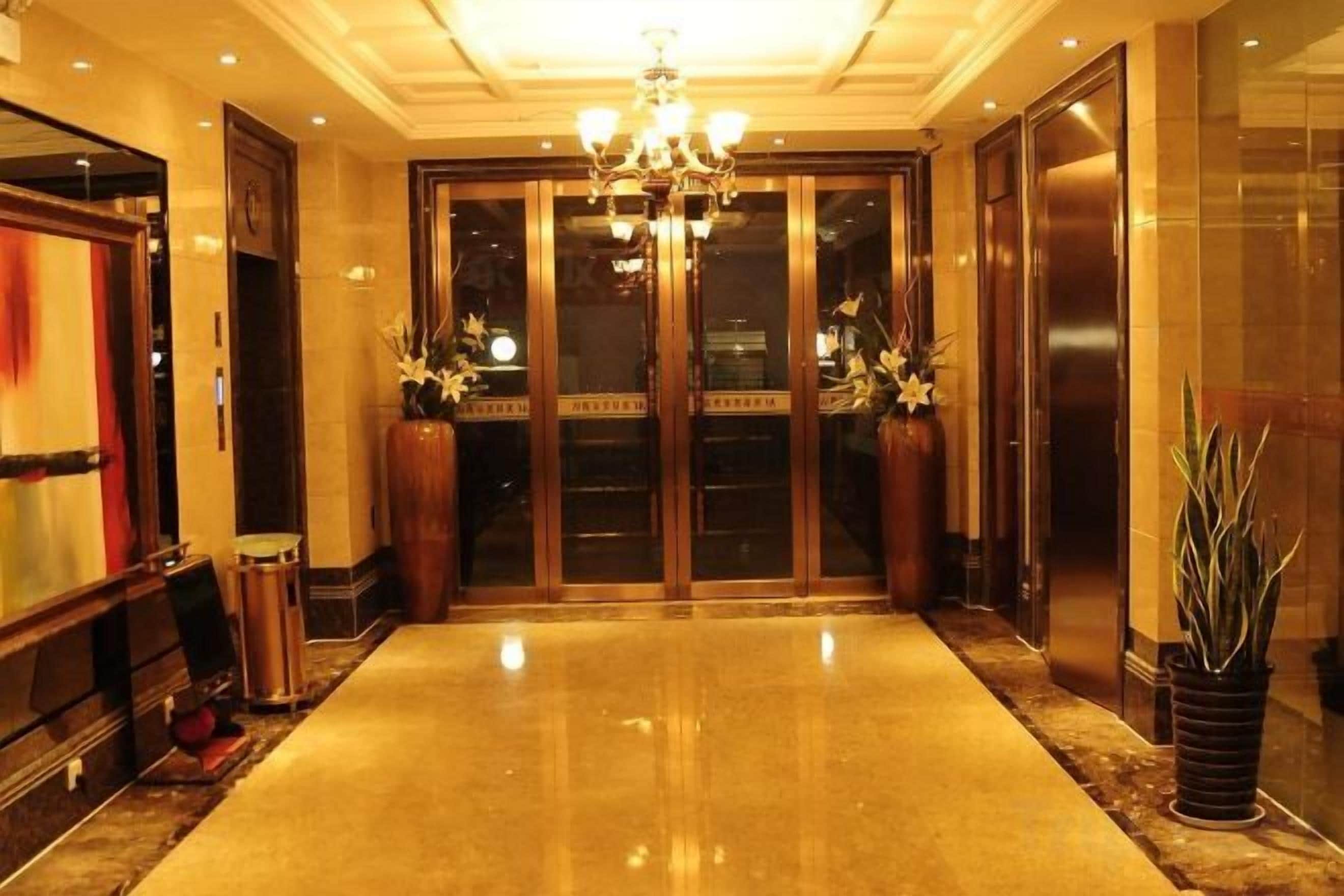 A hotel lobby with a chandelier, double doors, and potted plants.